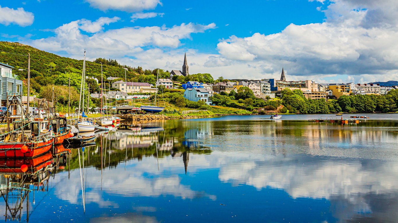 Pier at the port of Clifden at high tide, boats anchored with mirror reflection in the water