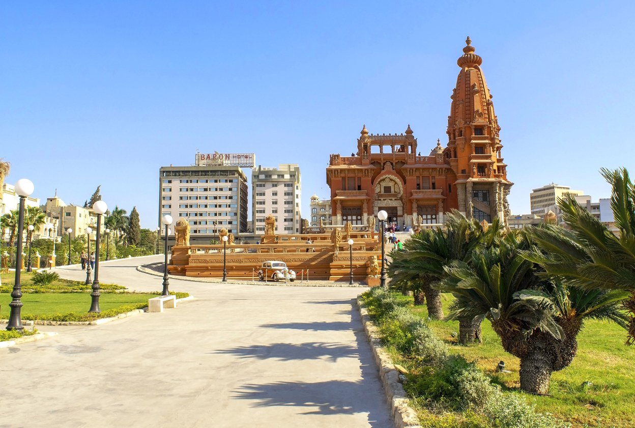 Misr al Gadida, Al Montaza, Beautiful view of Baron Empain palace with people and alley with palms during day. Le Palais Hindou temple