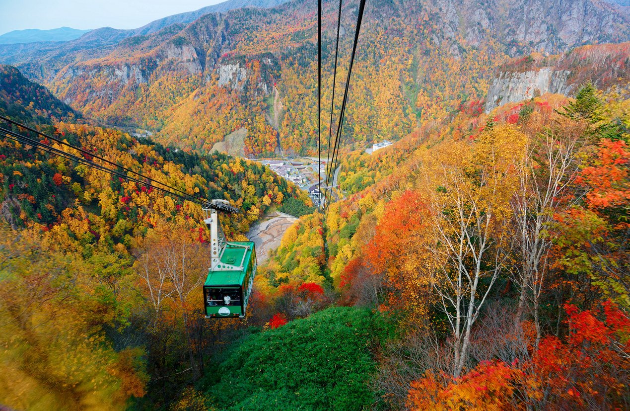 A breathtaking view from a cable car of Kurodake Ropeway flying over colorful autumn forests on the mountainside in Sounkyo Gorge (層雲峡) in Daisetsuzan (大雪山) National Park, in Kamikawa, Hokkaido Japan