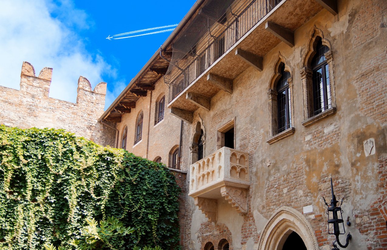 Romeo and Juliet balcony. Courtyard of Casa di Giulietta (House of Juliet or House of Cappelletti) against with Jet plane, Airliner in high flight with vapor trail.