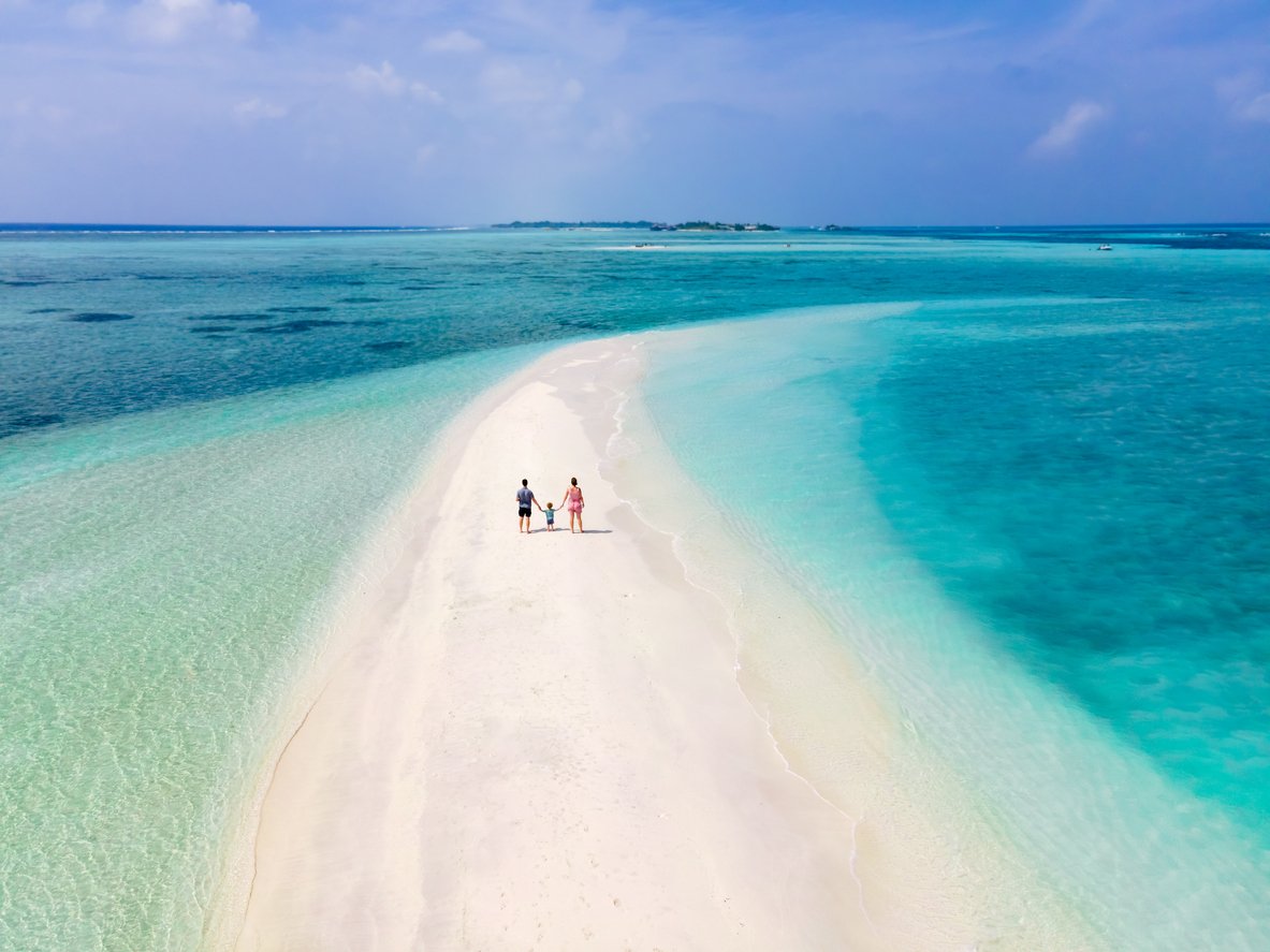 Family with toddler on beautiful beach spending holidays vacation travelling to tropical island with white sand, turquoise sea water and blue sky. Couple with small child walking together.